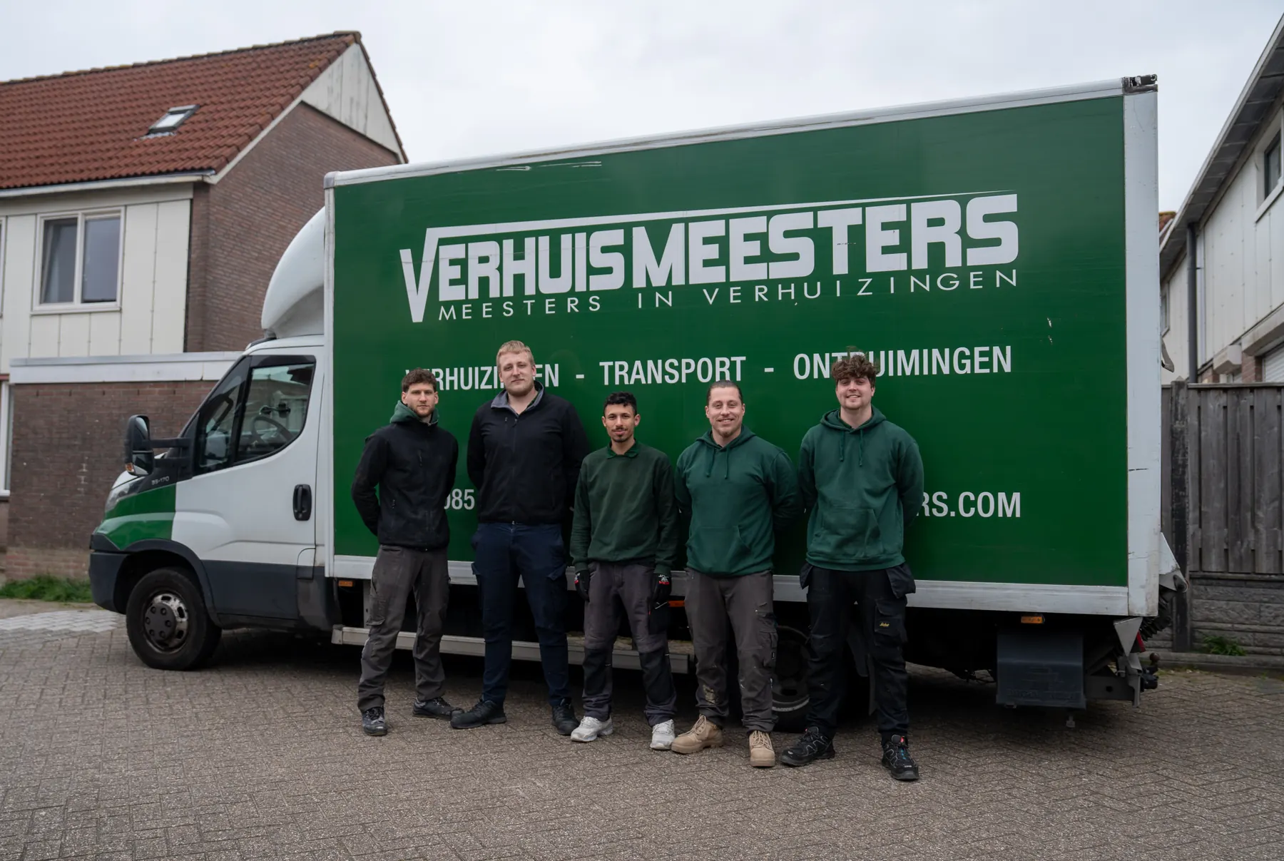 Verhuizers van VerhuisMeesters in werkkleding voor een groene verhuiswagen met het bedrijfslogo
