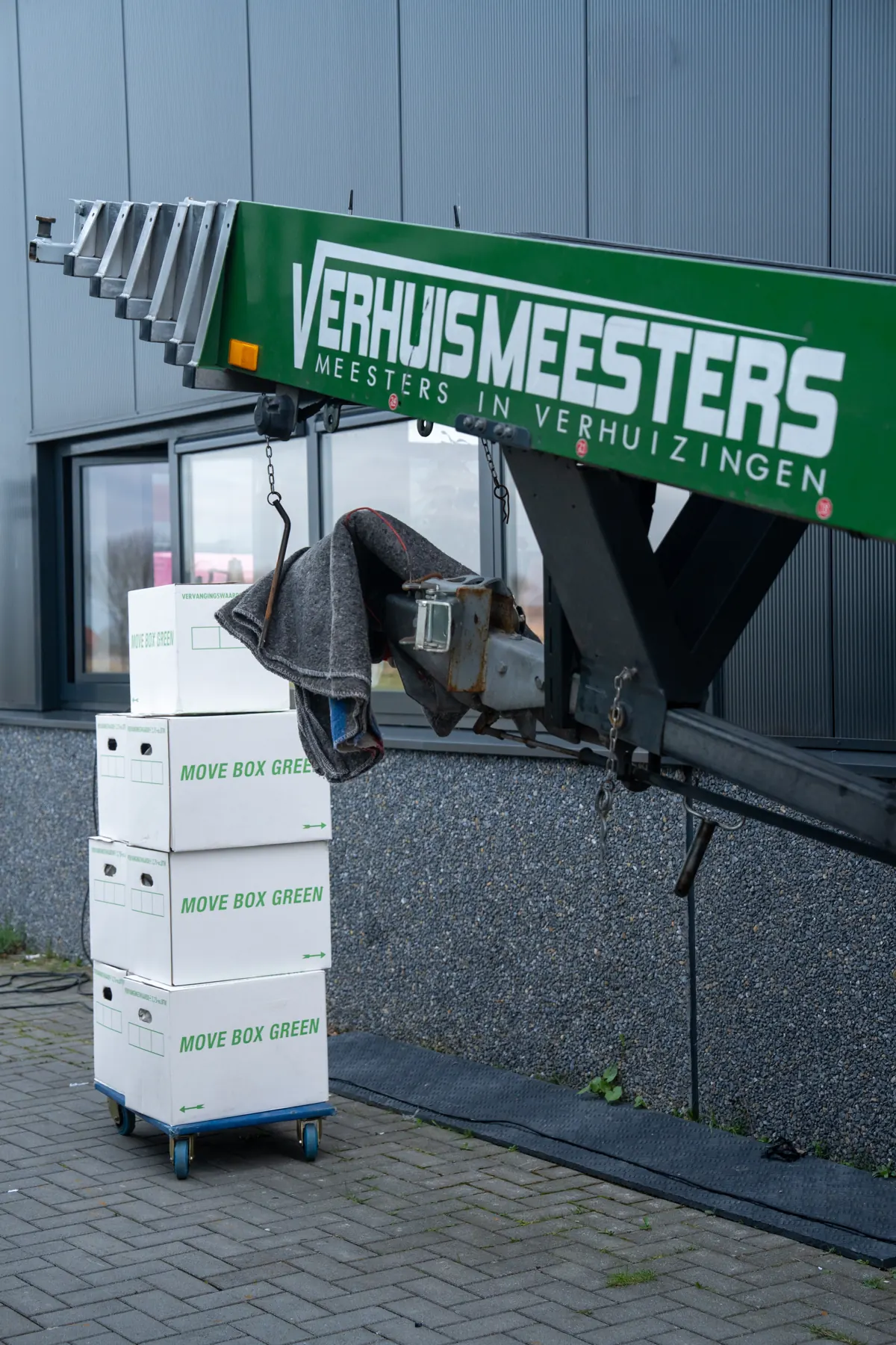 Groene verhuislift van VerhuisMeesters naast een stapel Move Box Green-dozen op een rolplateau