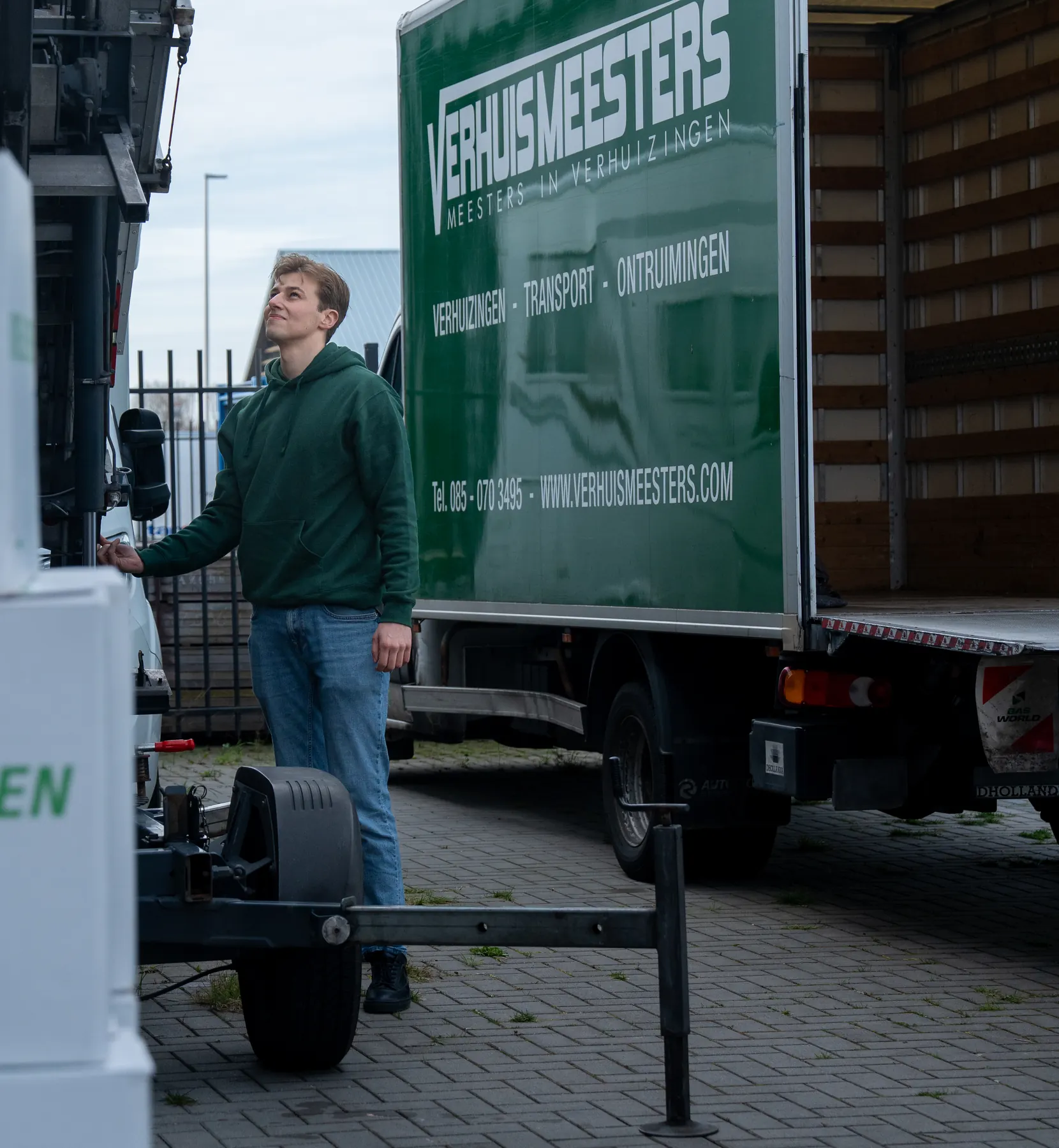Een verhuizer van VerhuisMeesters kijkt omhoog langs de verhuislift, naast een eigen wagen met open laadruimte